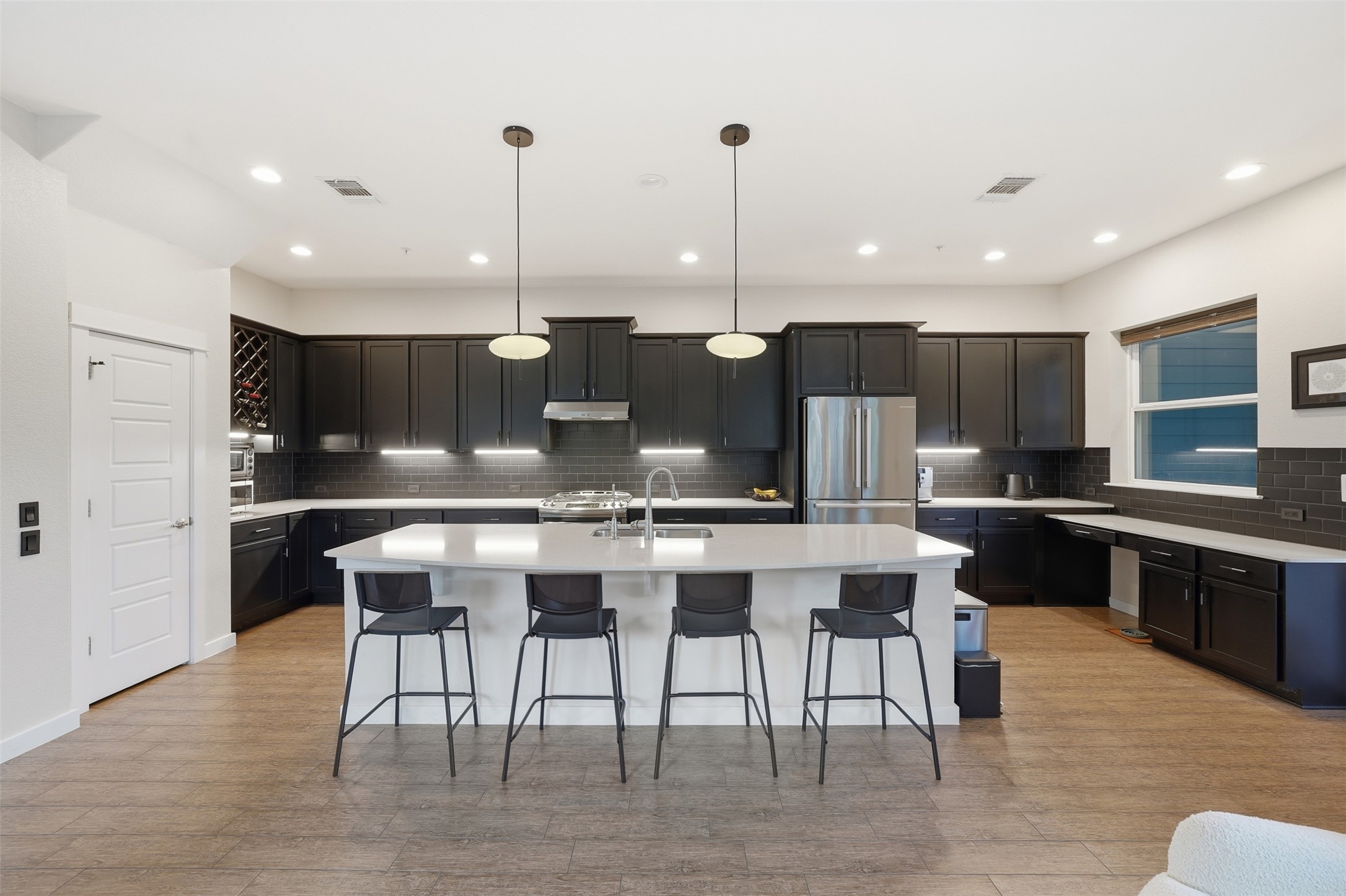 3901 Vaughan Street Austin, TX 78723 - Photo 9 of 37 Modern kitchen featuring a large central island with seating, dark cabinetry, stainless steel appliances, and wood-finish flooring