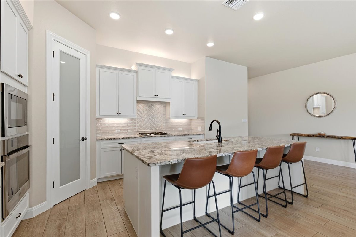 304 Morning Ridge Georgetown, TX 78628 - Photo 11 of 31 Kitchen featuring light stone counters, a breakfast bar area, stainless steel appliances, a kitchen island with sink, and light wood finished floors