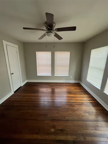 an empty room with wooden floor fan and windows
