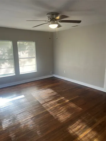 an empty room with wooden floor fan and windows