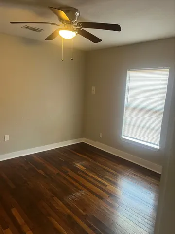an empty room with wooden floor fan and windows