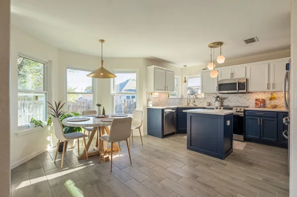 a kitchen with stainless steel appliances granite countertop a stove a refrigerator a kitchen island a dining table and chairs with wooden floor