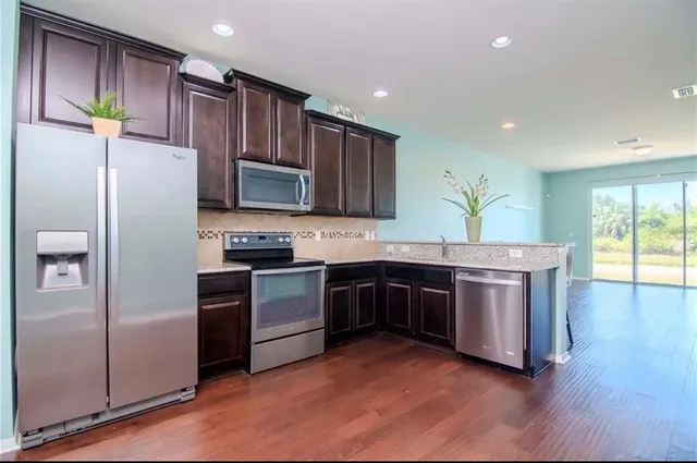a kitchen with granite countertop wooden floors stainless steel appliances and a window