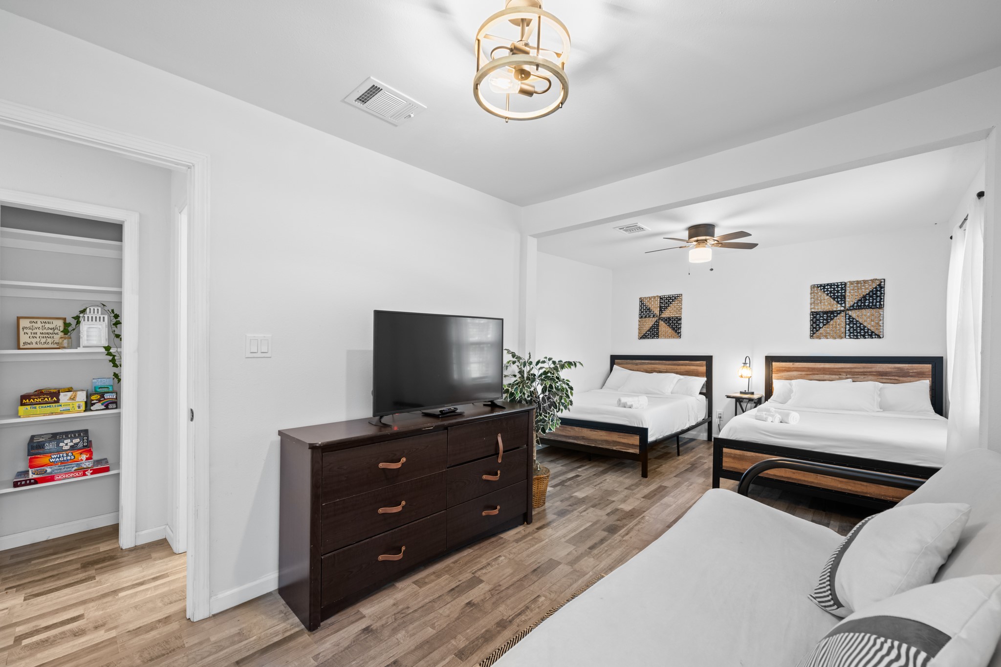729 Kyle Angleton, TX 77515 - Photo 28 of 36 This spacious bedroom features two large beds, a cozy sitting area, and a modern ceiling fan. The room is bright with natural light, has wood-look flooring, and includes a TV and dresser. A built-in shelf provides extra storage space.