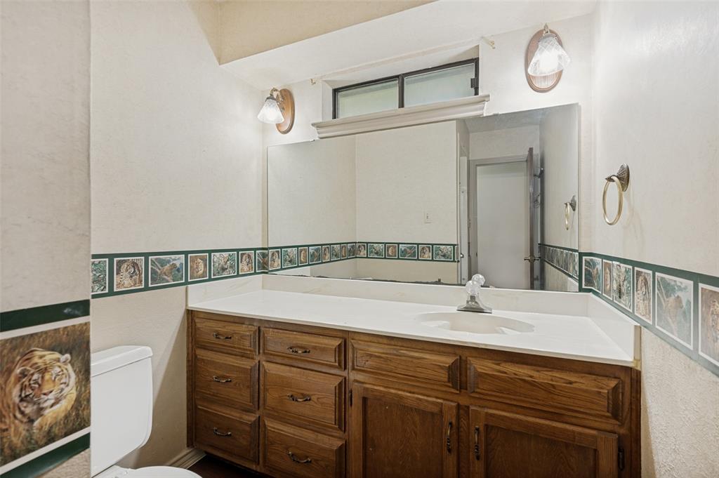508 South Pedigo Street Pilot Point, TX 76258 - Photo 18 of 26 Bathroom vanity featuring a wood-finish cabinet, white countertop with integrated sink, and an expansive wall-mounted mirror