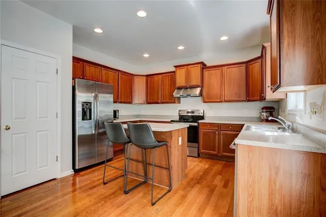 a kitchen with stainless steel appliances granite countertop wooden cabinets a sink a stove a refrigerator and island with wooden floor