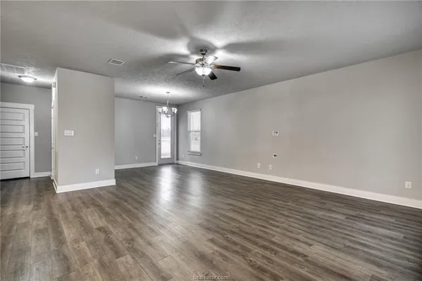 a view of an empty room with wooden floor and a ceiling fan