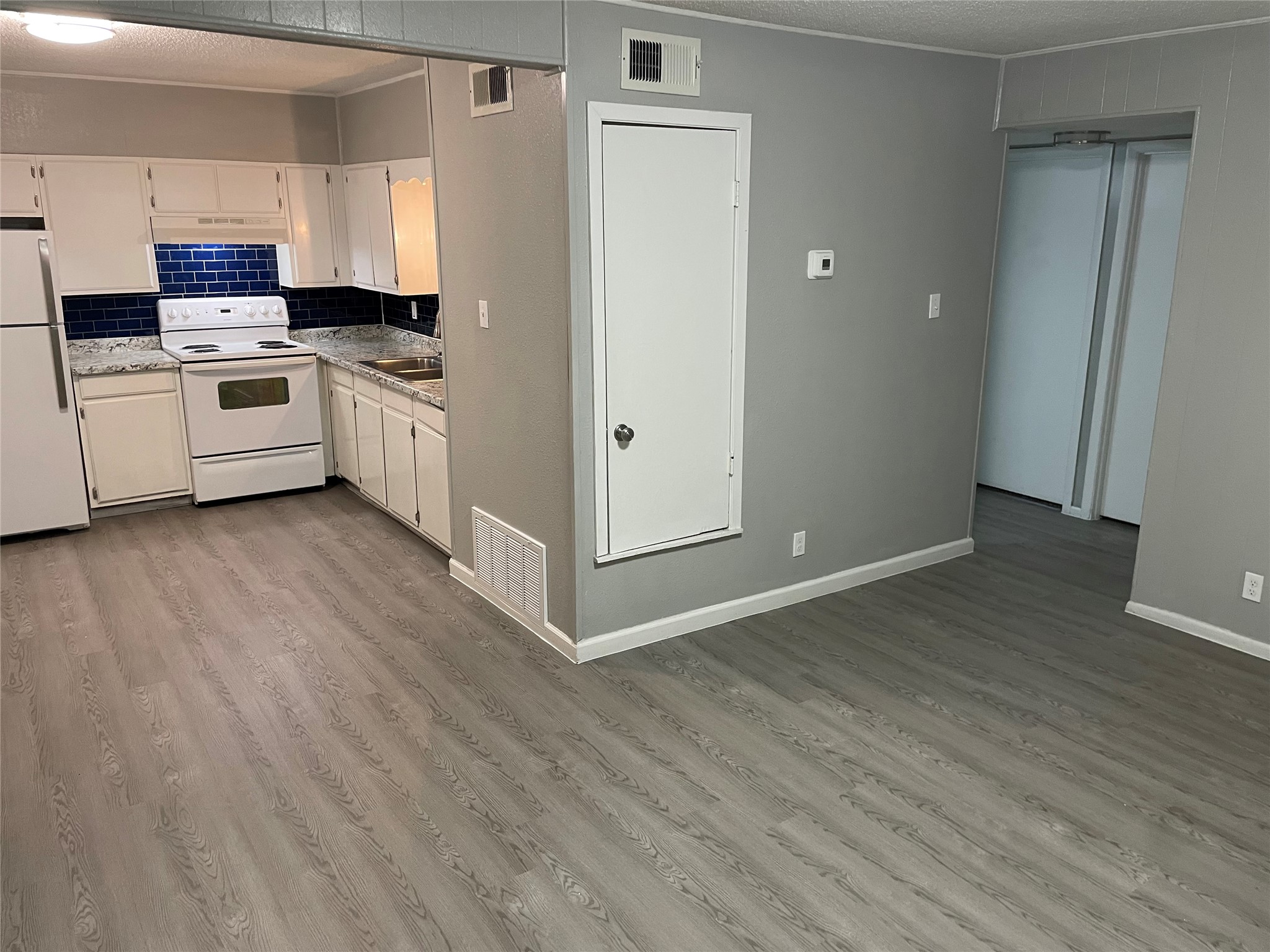 1209 Vance Street, Unit 45 Taylor, TX 76574 - Photo 4 of 32 Kitchen featuring white appliances, a textured ceiling, decorative backsplash, light wood finished floors, and white cabinets