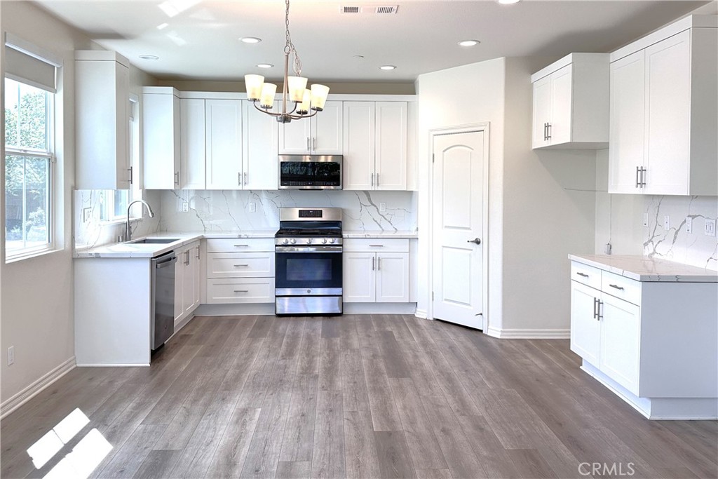 9318 Hellman Avenue, Unit 4 Rancho Cucamonga, CA 91730 - Photo 5 of 28 a kitchen with stainless steel appliances a stove a sink dishwasher a refrigerator white cabinets and wooden floor