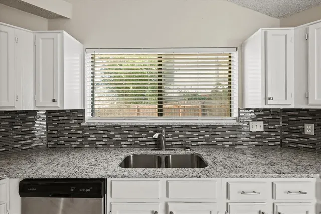 a kitchen with granite countertop a sink and a white wooden cabinets