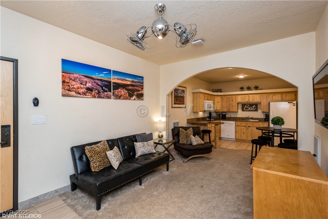 Living area featuring a textured ceiling, arched walkways, a notable chandelier, and light colored carpet
