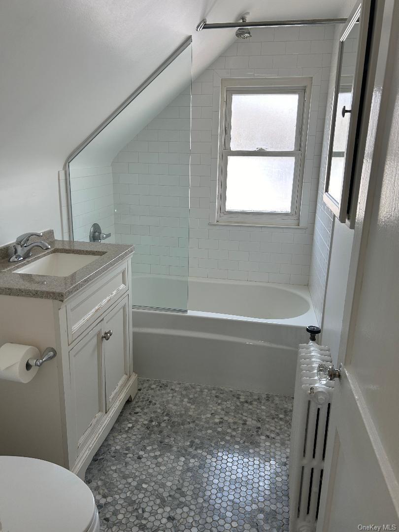 19 Firwood Road, Unit 2 Port Washington, NY 11050 - Photo 6 of 9 Bathroom with radiator heating unit, tile patterned flooring, toilet, vanity, and tub / shower combination