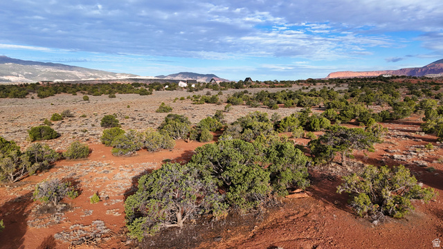 358 South Sky Drive Torrey, UT 84775 - Photo 56 of 82 Expansive desert landscape featuring red earth and scattered green shrubbery, with distant mountain ranges and a distinct rock formation under a partly cloudy sky