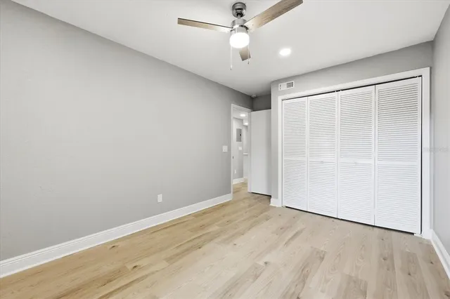 an empty room with wooden floor fan and windows