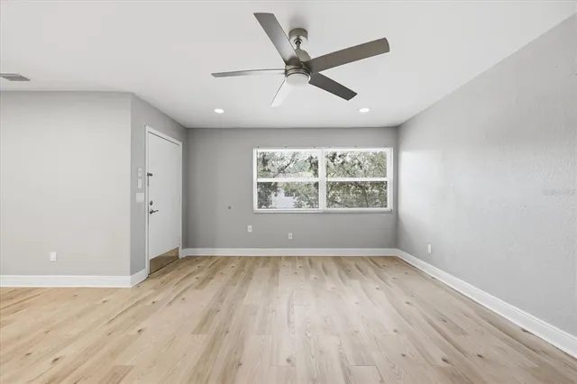 an empty room with wooden floor windows and fan
