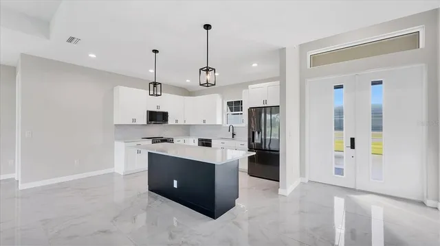 a kitchen with stainless steel appliances kitchen island granite countertop a refrigerator a stove oven and white cabinets with wooden floor