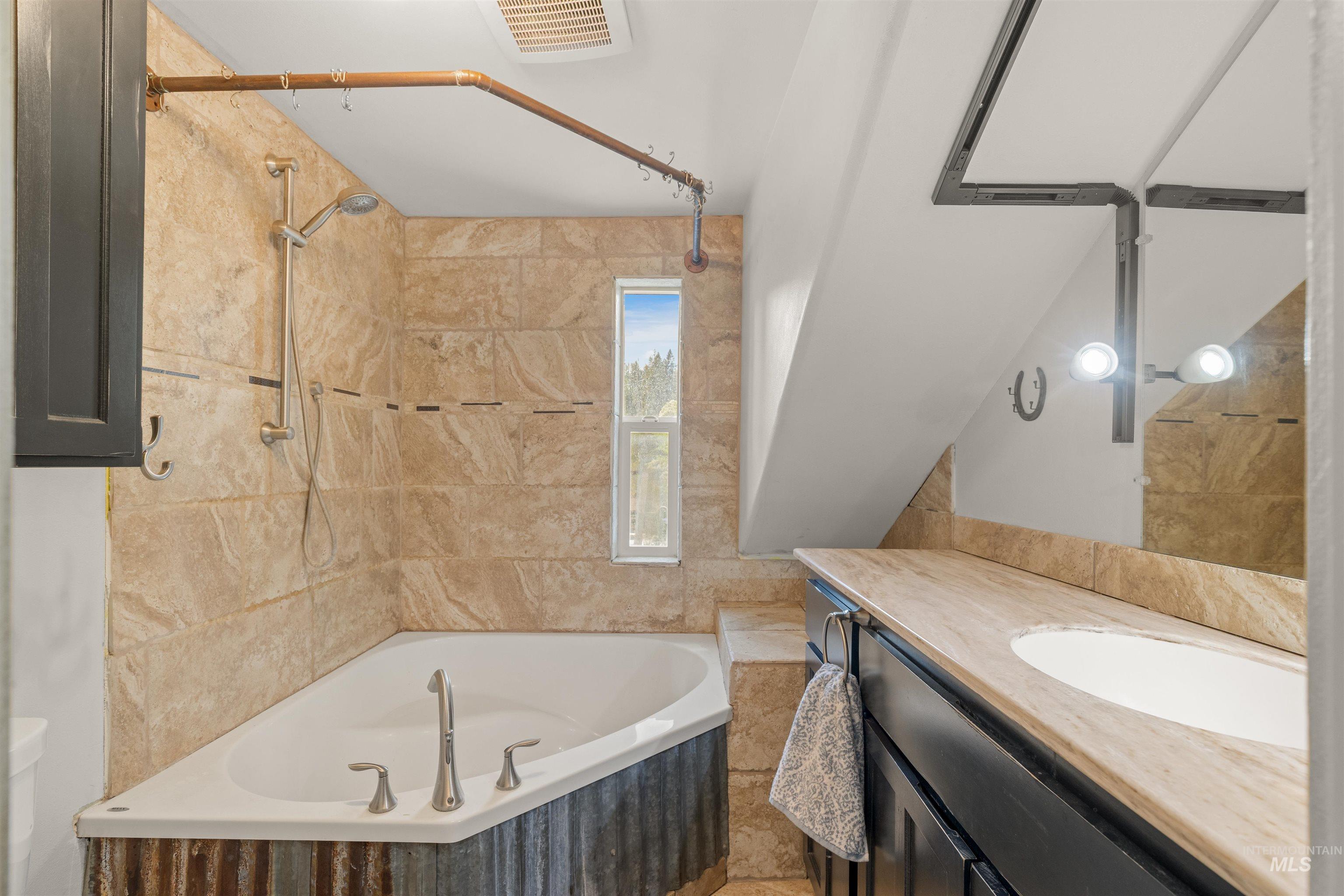 1314 Cedar Ridge Road Kendrick, ID 83537 - Photo 29 of 50 Corner soaking tub with textured metal paneling, complemented by a handheld shower fixture