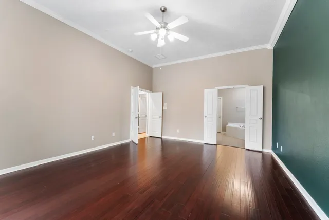 a view of an empty room with wooden floor and a ceiling fan
