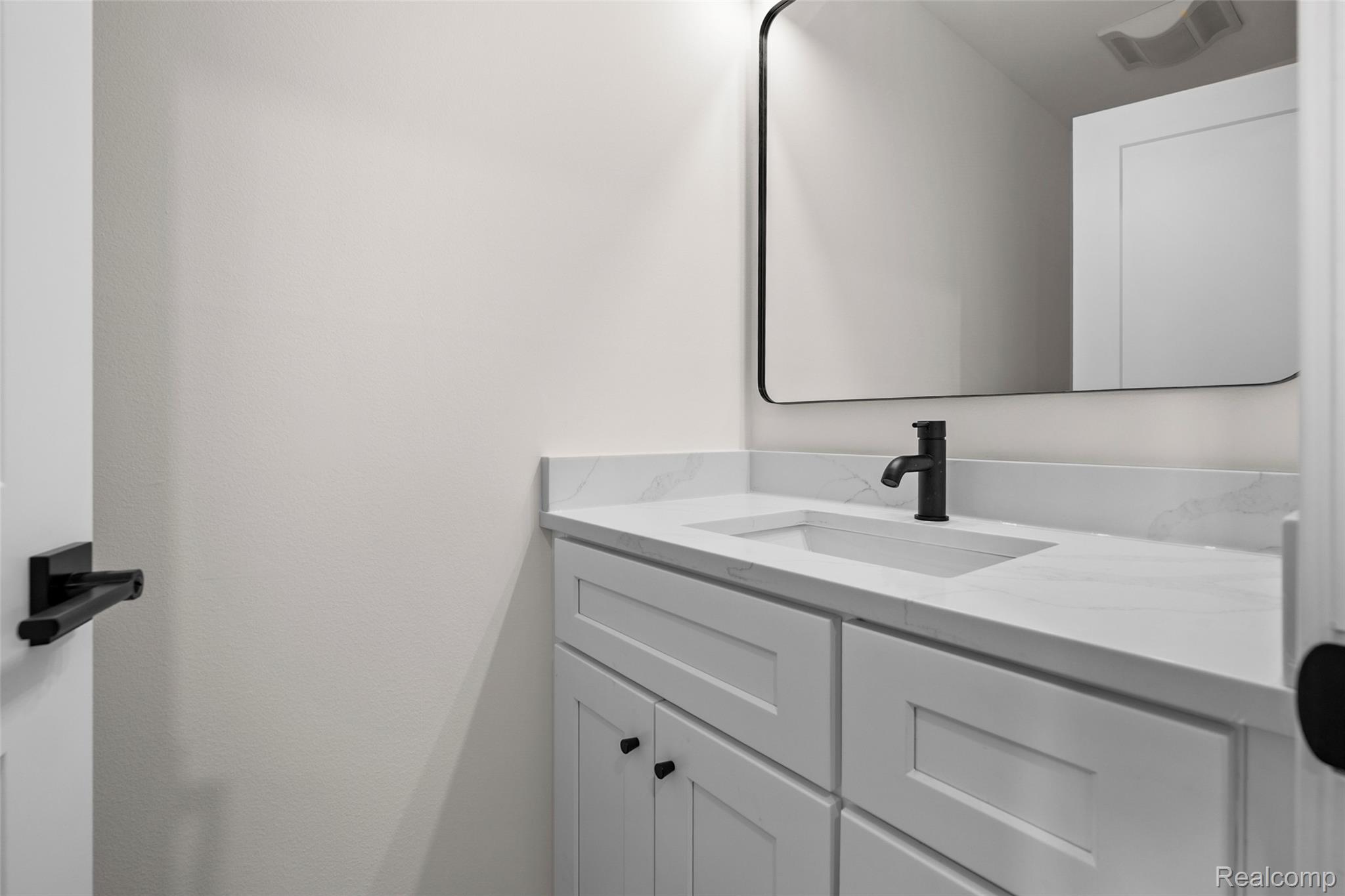 1830 Streamedge Court Rochester, MI 48309 - Photo 5 of 33 White shaker-style cabinetry with matte black hardware, integrated rectangular sink, stone-look countertop, and a contemporary black-framed mirror