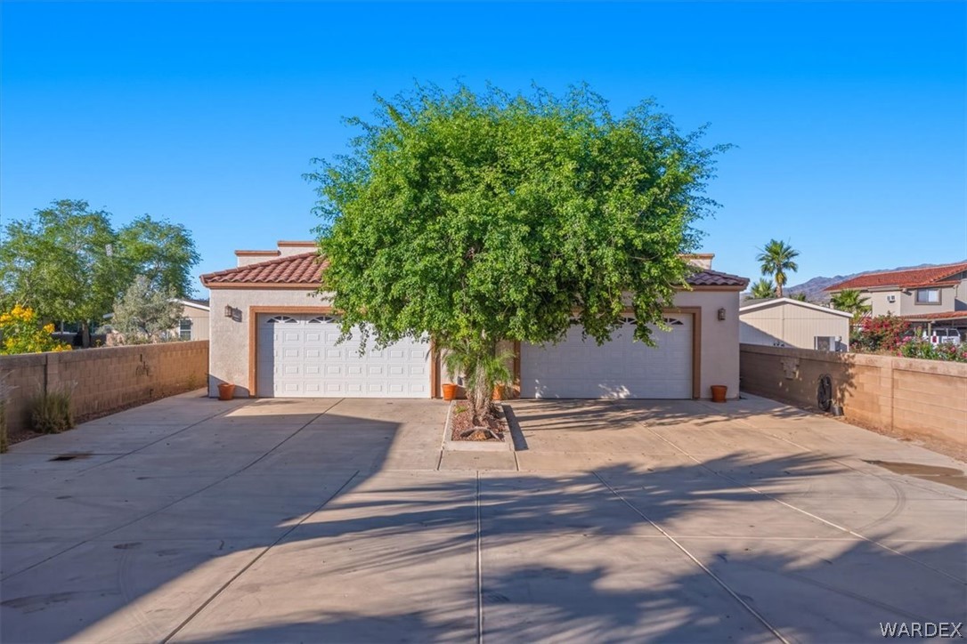 1084 Dike Road Mohave Valley, AZ 86440 - Photo 37 of 75 Mediterranean-style architecture with a terracotta tile roof, two white panel garage doors, and a mature tree at the center of the driveway