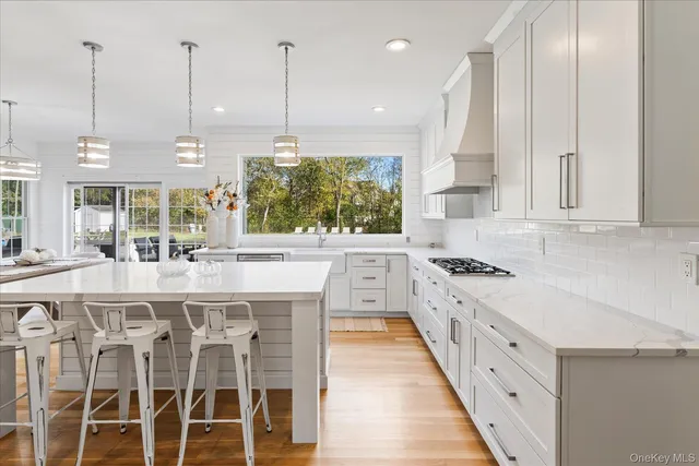 an open kitchen with granite countertop a stove a sink and white cabinets with wooden floor