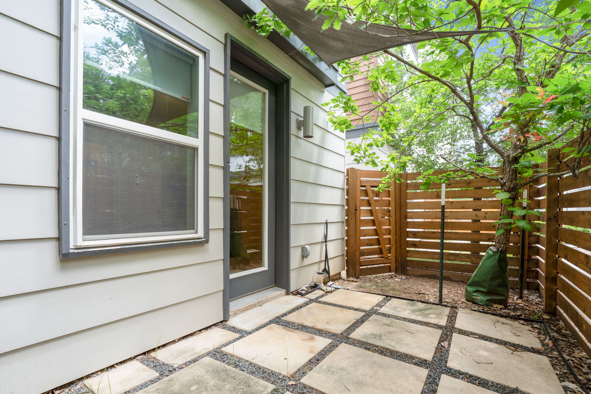 4403 Swift Path Austin, TX 78741 - Photo 25 of 32 Rear patio featuring a modern full-light door, horizontal wood fencing, mature tree, and paver and gravel hardscaping