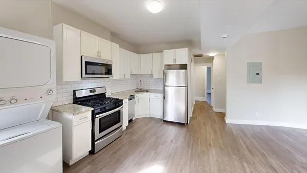 a kitchen with stainless steel appliances a refrigerator stove a sink and white cabinets with wooden floor