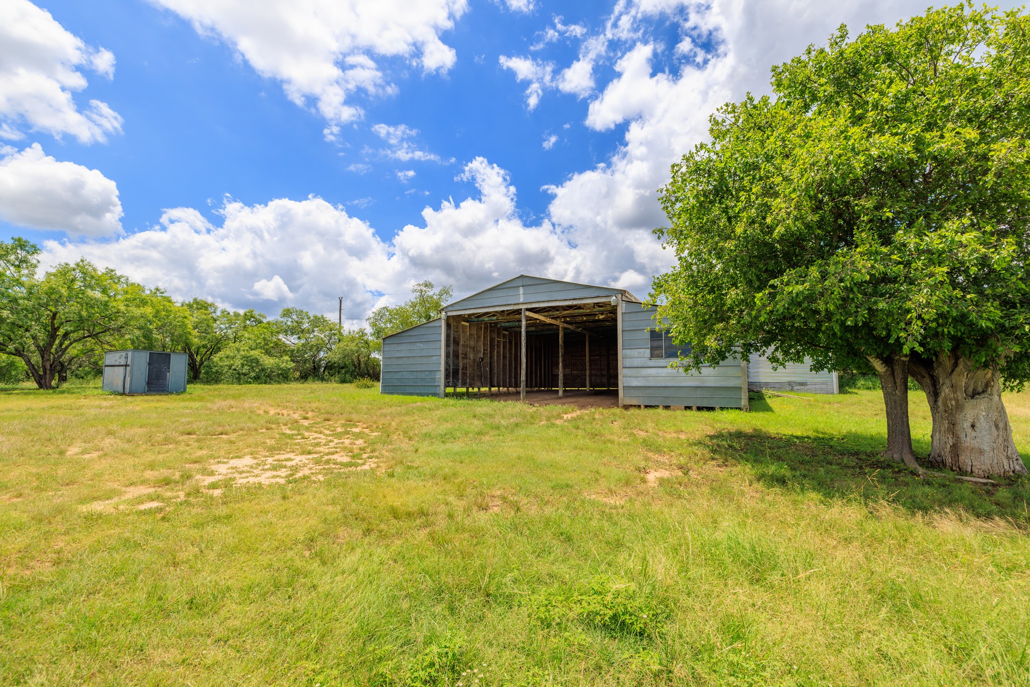 341 River View Road Fredericksburg, TX 78624 - Photo 6 of 40 A spacious outbuilding sits nestled among mature trees on a sprawling grassy lot.