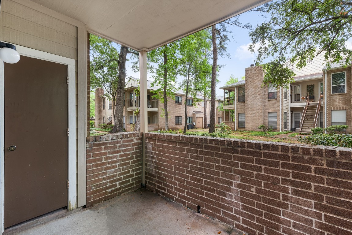 3500 Tangle Brush Drive, Unit 193 Spring, TX 77381 - Photo 22 of 26 Cozy covered patio with brick walls overlooking a peaceful courtyard and neighboring apartment buildings, offering a private outdoor space with a view of trees and greenery.