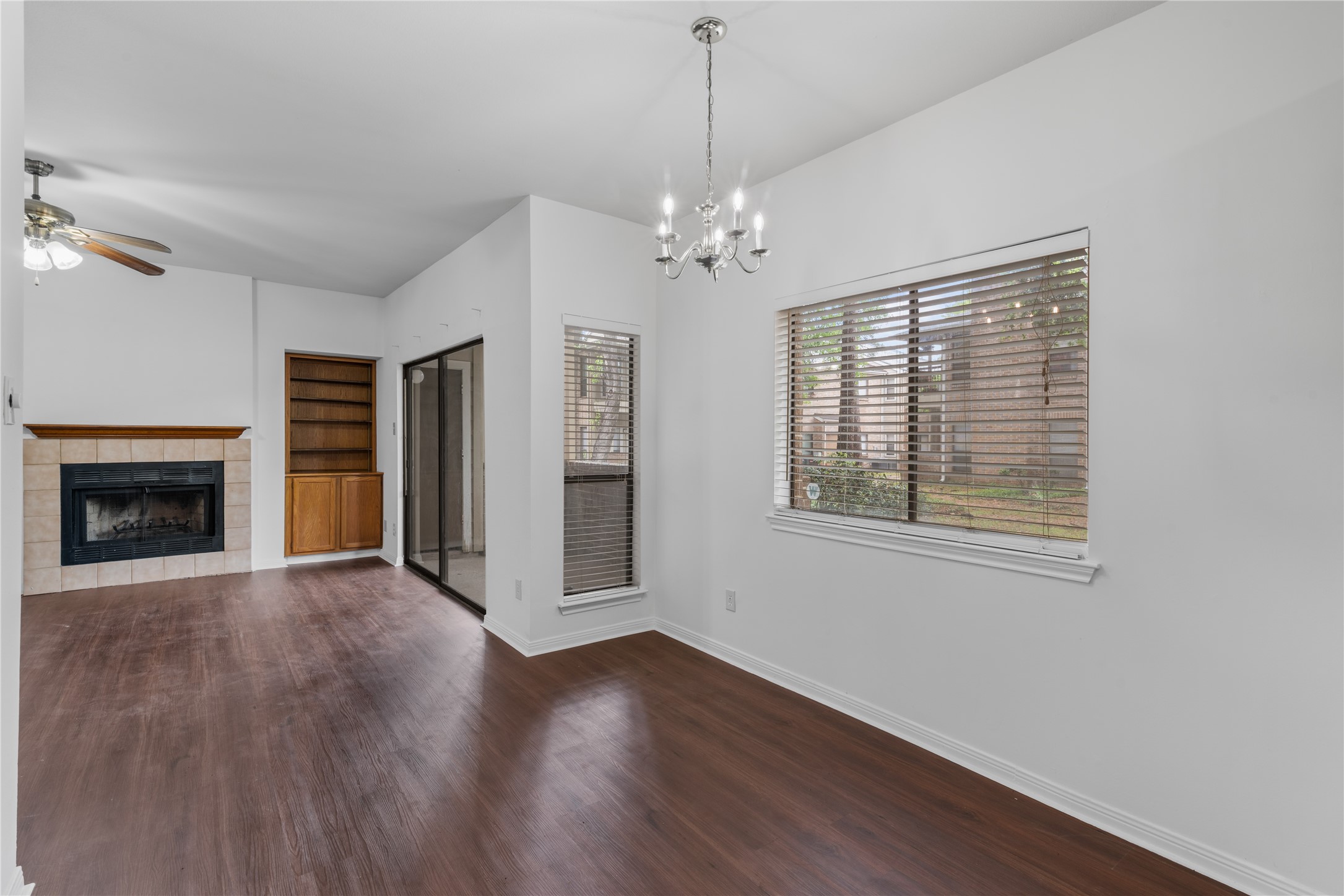 3500 Tangle Brush Drive, Unit 193 Spring, TX 77381 - Photo 3 of 26 Open living area with hardwood floors, a cozy fireplace, and built-in shelving. It features large windows for natural light and a sliding glass door leading to an outdoor space. The room has a modern ceiling fan and a stylish chandelier for added elegance.