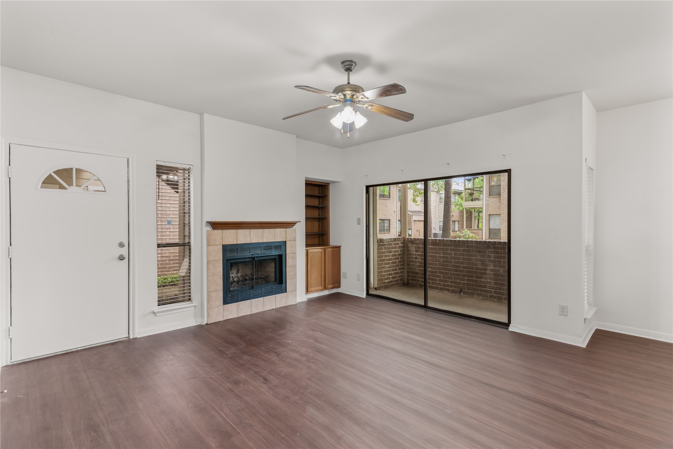3500 Tangle Brush Drive, Unit 193 Spring, TX 77381 - Photo 4 of 26 Extra space for living room features a cozy fireplace, ceiling fan, and sliding glass doors leading to a private balcony. The space has wood-style flooring and a built-in shelf, creating a welcoming and functional area.