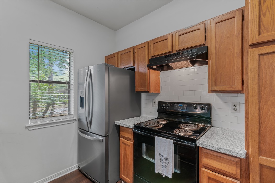 3500 Tangle Brush Drive, Unit 193 Spring, TX 77381 - Photo 8 of 26 Long wide kitchen features stainless steel appliances, including a French door refrigerator and an electric stove. It has wooden cabinets, granite countertops, and a white subway tile backsplash. A window provides natural light and a view of greenery.