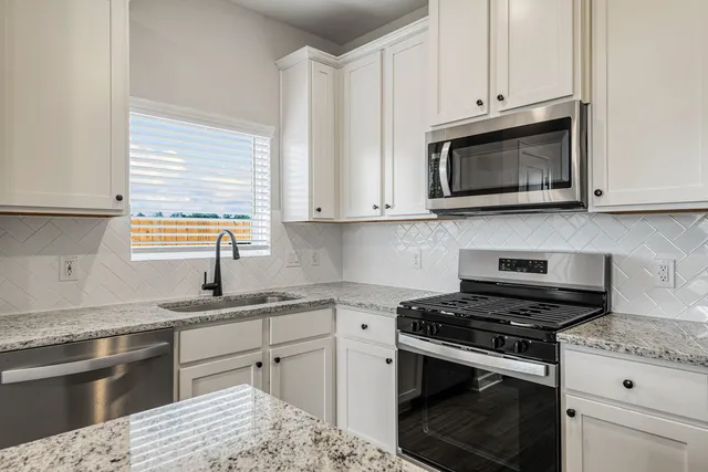 a kitchen with granite countertop white cabinets appliances and a window