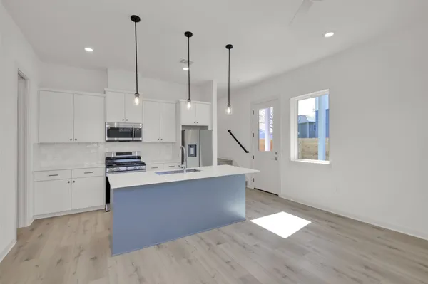 a kitchen with stainless steel appliances kitchen island a stove a refrigerator a sink and white cabinets with wooden floor