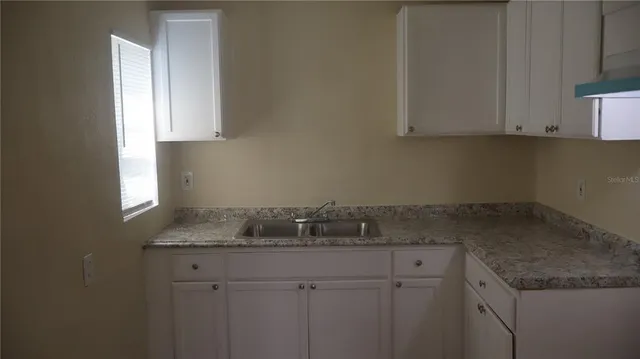 a sink with granite countertop white cabinets and a window