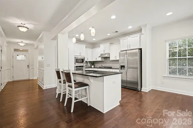 a kitchen with stainless steel appliances a refrigerator a stove a sink dishwasher and a dining table with wooden floor