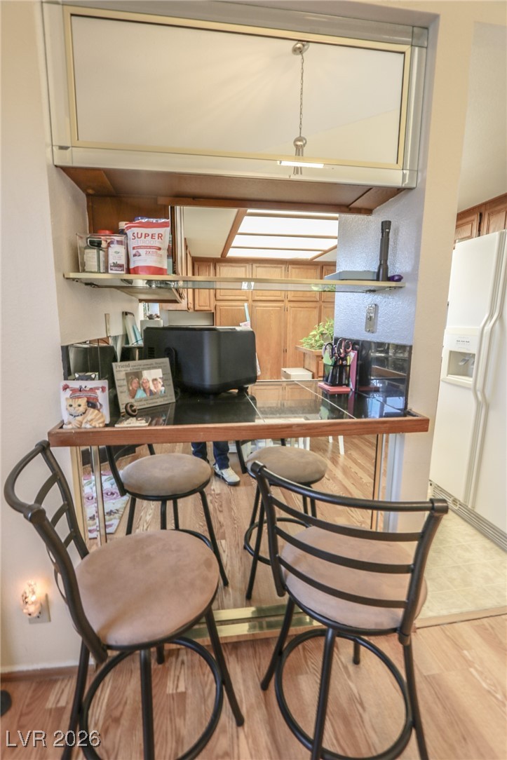 3201 La Mancha Way Henderson, NV 89014 - Photo 13 of 43 Kitchen featuring dark countertops, light wood-type flooring, white refrigerator with ice dispenser, and a kitchen bar