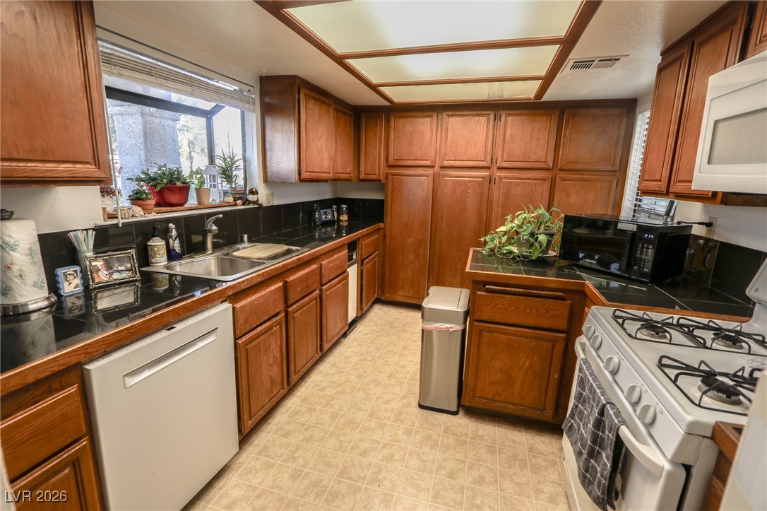 3201 La Mancha Way Henderson, NV 89014 - Photo 7 of 43 Kitchen featuring brown cabinetry, white appliances, light flooring, and tile counters