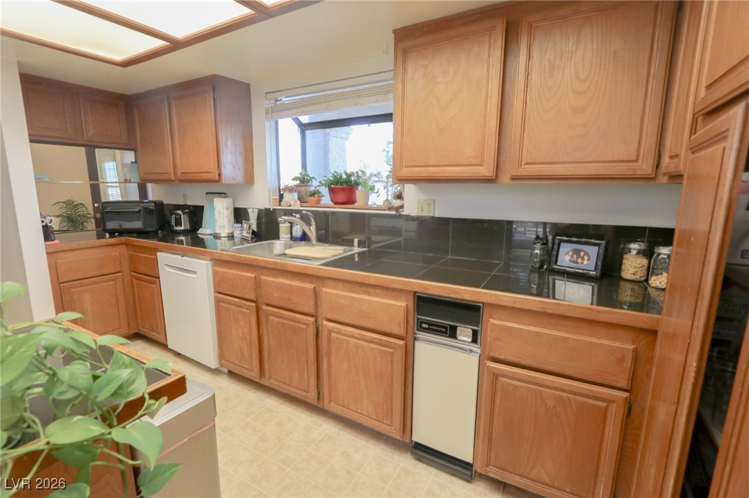 3201 La Mancha Way Henderson, NV 89014 - Photo 9 of 43 Kitchen with white dishwasher, dark countertops, brown cabinetry, and light flooring