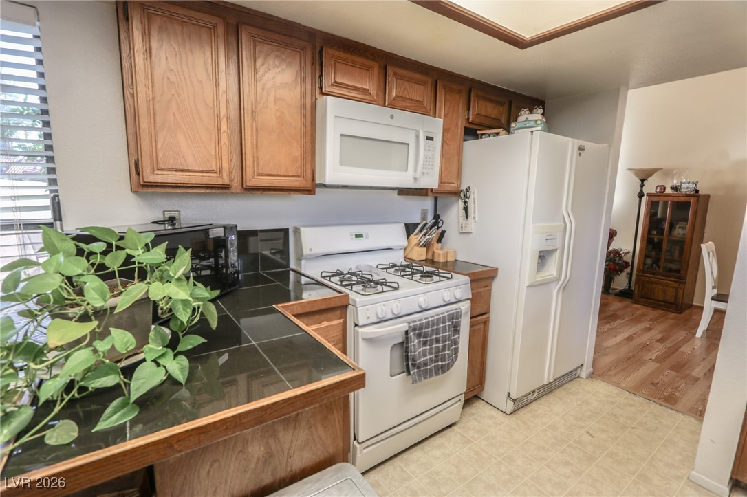 3201 La Mancha Way Henderson, NV 89014 - Photo 10 of 43 Kitchen with brown cabinetry, white appliances, and tile counters