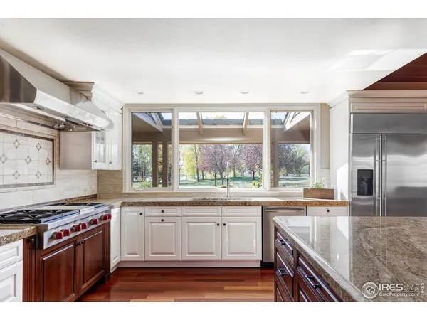 a kitchen with stainless steel appliances granite countertop a stove a sink and a granite counter tops with white cabinets next to a window