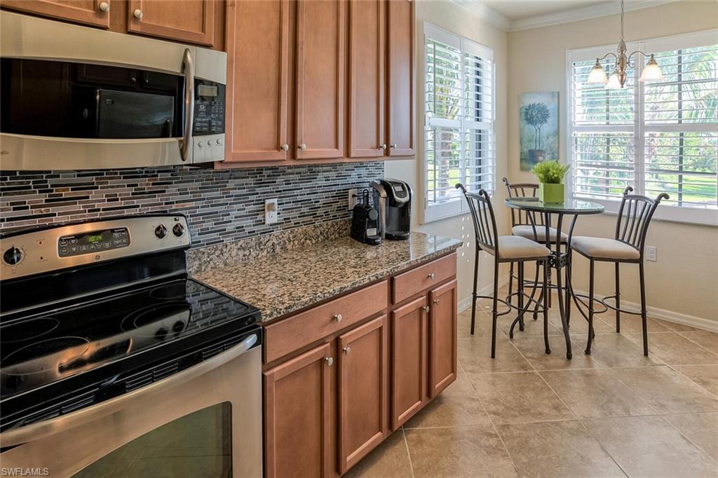 9719 Acqua Court, Unit 228 Naples, FL 34113 - Photo 8 of 35 a kitchen with stainless steel appliances kitchen island granite countertop a stove a sink and a microwave