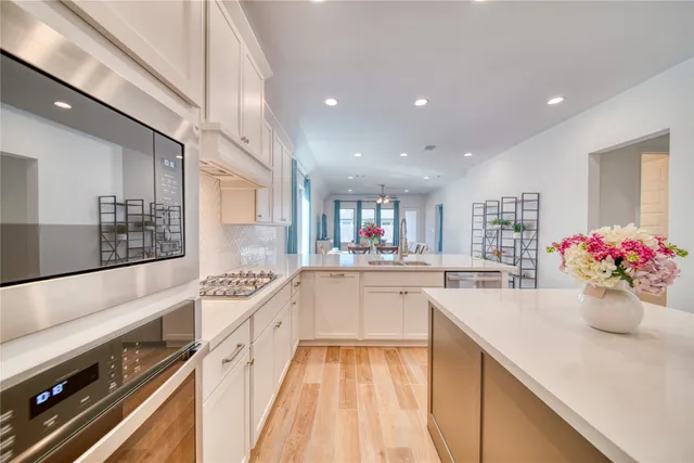 a large white kitchen with stainless steel appliances granite countertop a lot of counter space and wooden floors