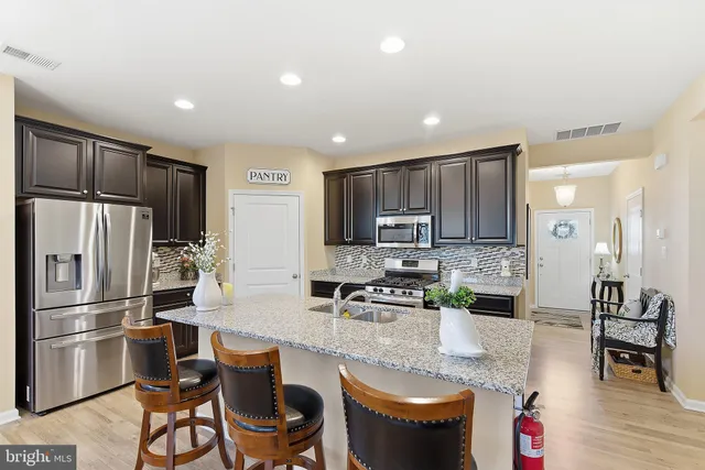 a kitchen with stainless steel appliances granite countertop a refrigerator a stove a sink a dining table and chairs with wooden floor