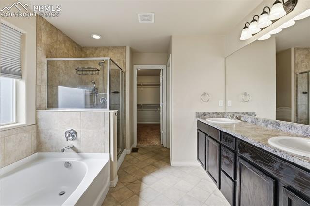 2224 Reed Grass Way Colorado Springs, CO 80915 - Photo 30 of 39 Bathroom with a bath, a walk in closet, double vanity, a stall shower, and light tile patterned flooring