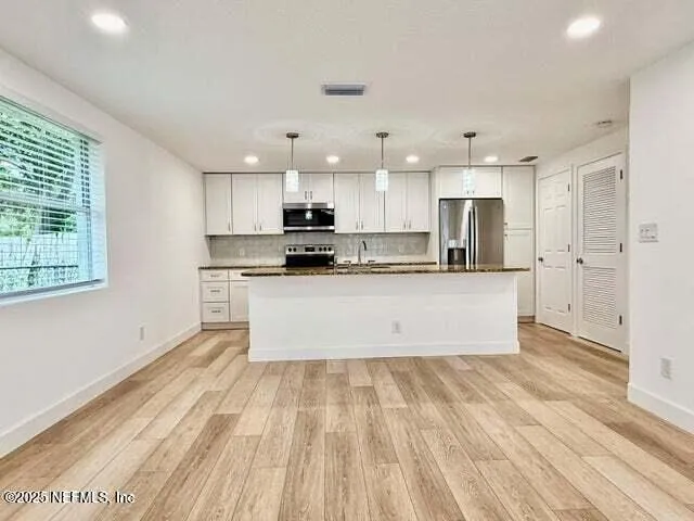 a large kitchen with kitchen island a stove a sink dishwasher a refrigerator and white cabinets with wooden floor