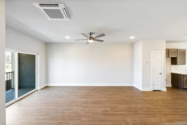 a view of an empty room with wooden floor and a ceiling fan