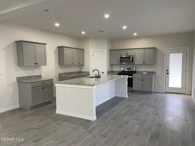 a large kitchen with stainless steel appliances granite countertop a stove a sink a refrigerator and white cabinets with wooden floor