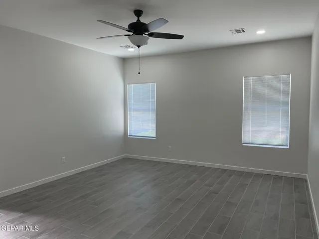 an empty room with wooden floor chandelier fan and windows