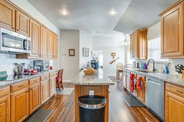 a kitchen with stainless steel appliances granite countertop a stove a sink dishwasher and a refrigerator with wooden cabinets